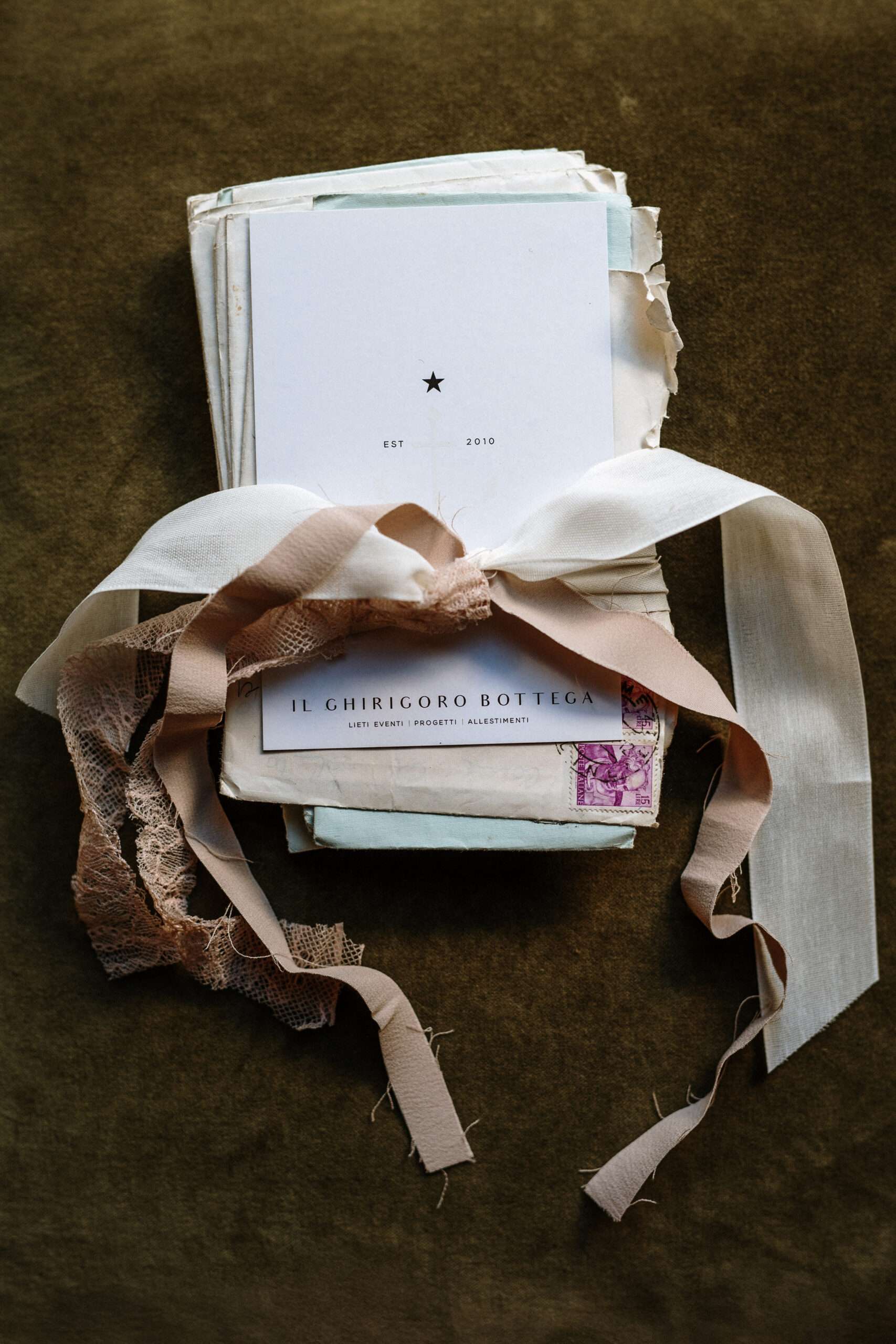 un fascio di lettere vintage con sopra una cartolina del ghirigoro bottega legate con nastri di recupero rosa cipria